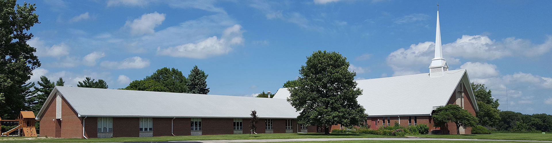 Wide angle showing the outside of the church, a small playground, and a large lawn