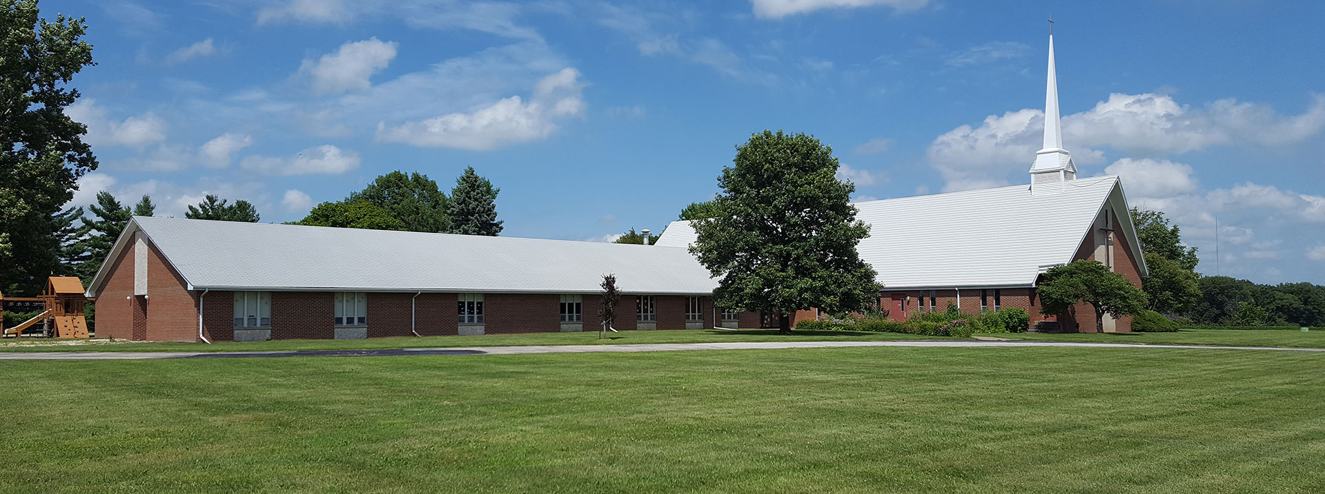Wide angle showing the outside of the church, a small playground, and a large lawn