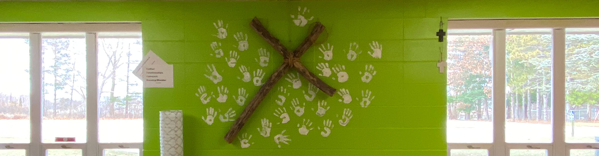 Wide angle showing a cross of wood and children's hand-prints on a green wall